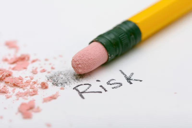 Yellow pencil eraser rubbing out the word risk on white paper