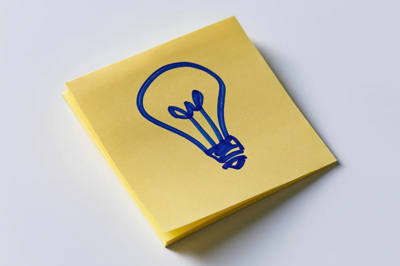 Yellow sticky note with hand-drawn blue lightbulb on white surface
