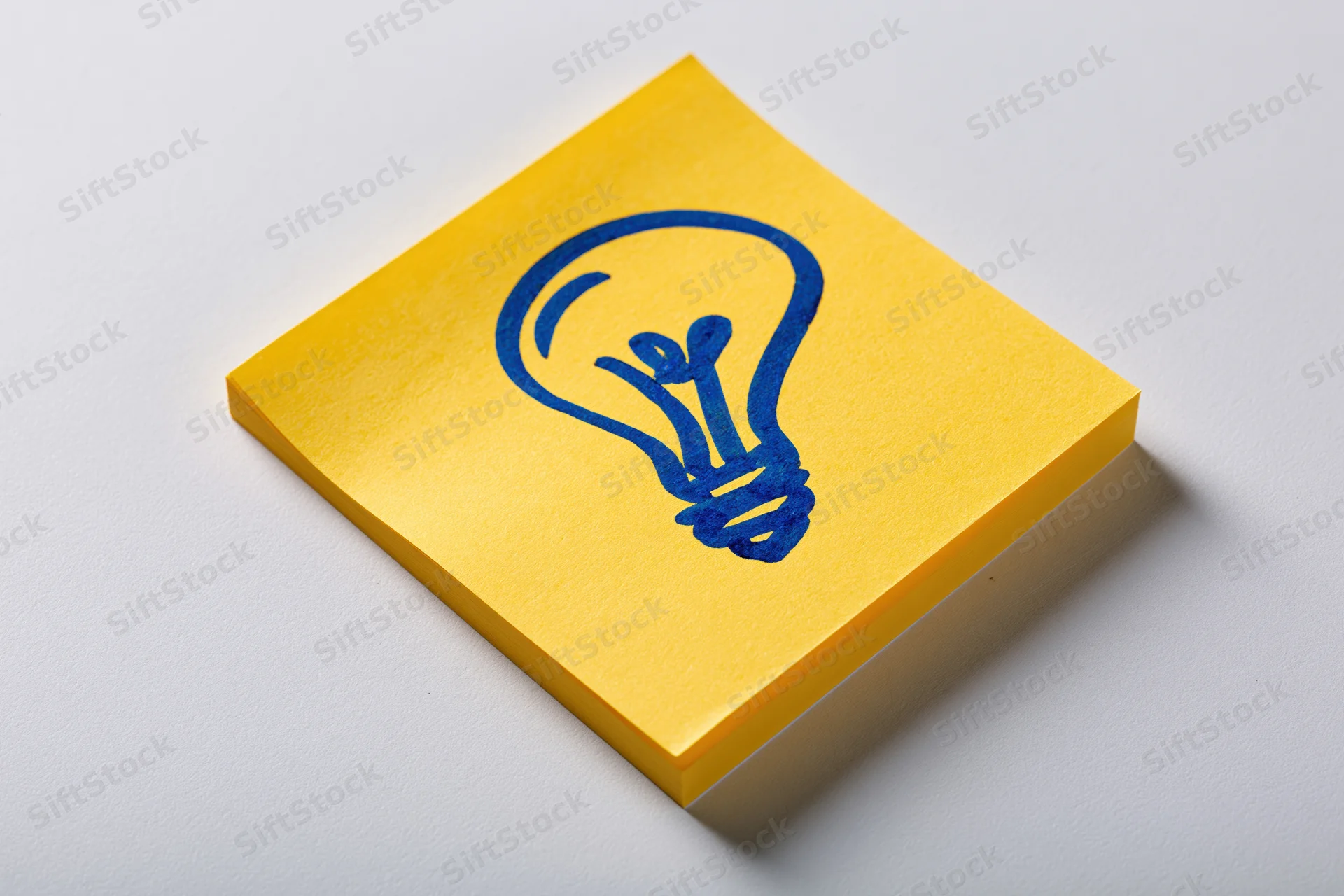 Yellow sticky note with hand-drawn blue lightbulb on white surface