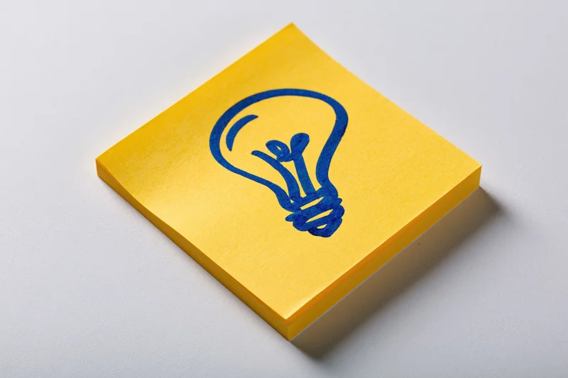 Yellow sticky note with hand-drawn blue lightbulb on white surface