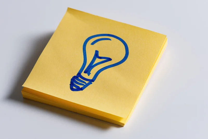 Yellow sticky note with hand-drawn blue lightbulb on white surface