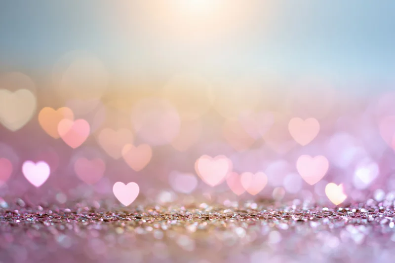 Heart-shaped bokeh lights over glittery pink surface with soft focus background