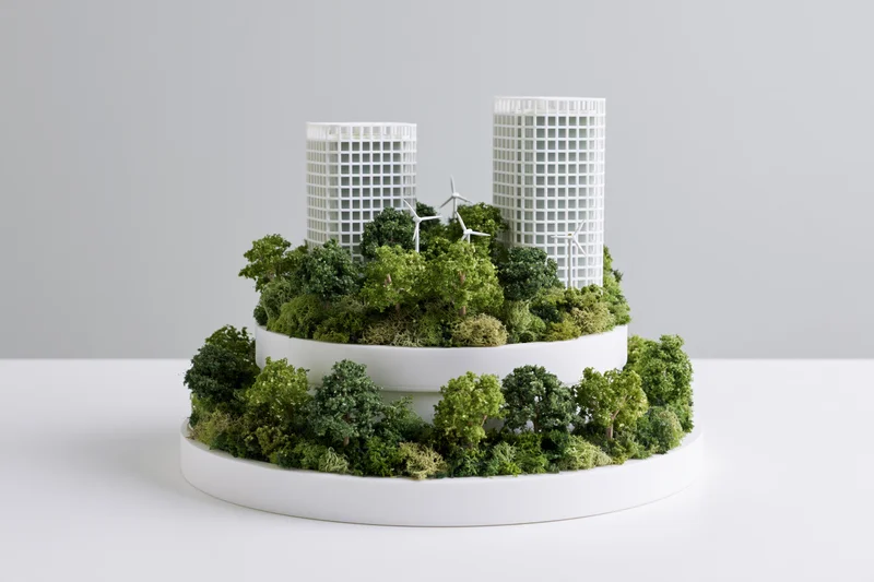 Tiered architectural model of a sustainable green city with trees and wind turbines on white platforms