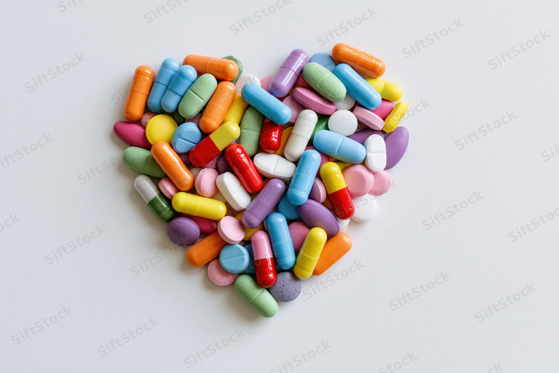 Colorful pills and capsules arranged in heart shape on white surface