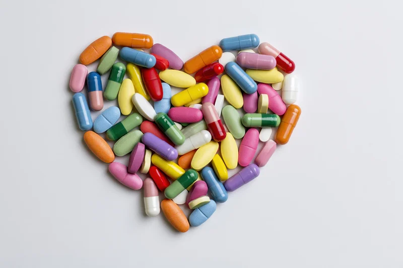 Colorful pills and capsules arranged in heart shape on white background