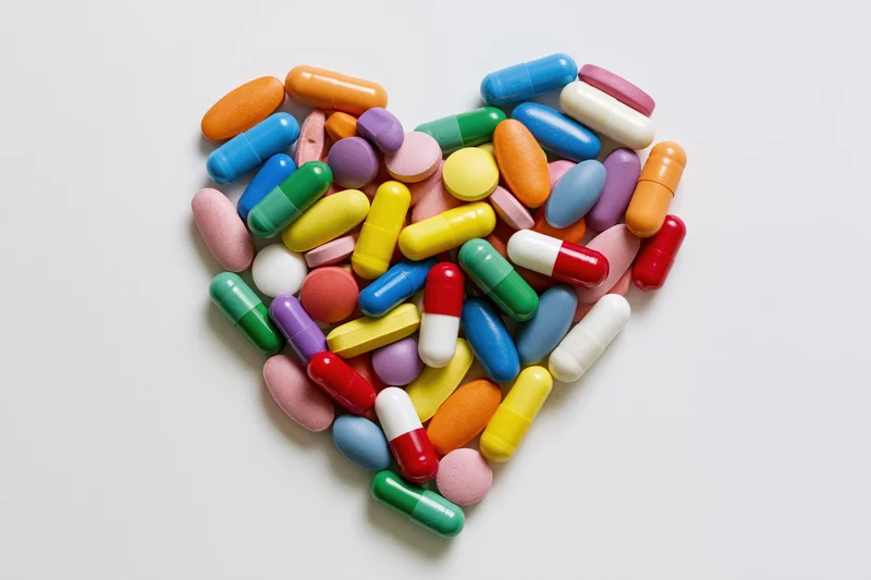Colorful pills and capsules arranged in a heart shape on white background