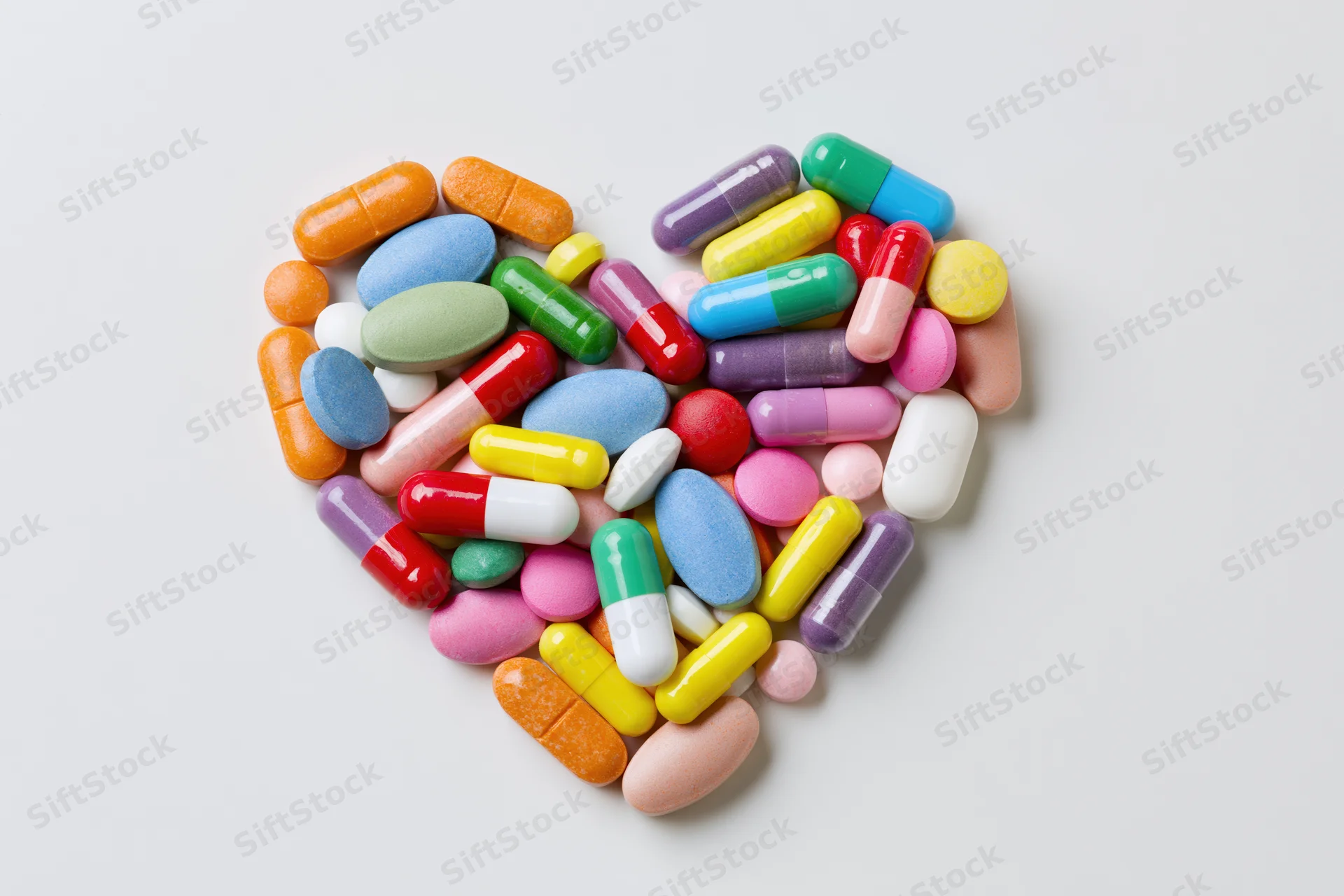 Colorful pills and capsules arranged in a heart shape on white background