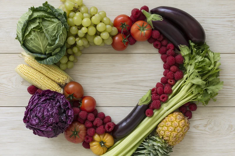 Heart-shaped arrangement of fresh fruits and vegetables on wooden surface
