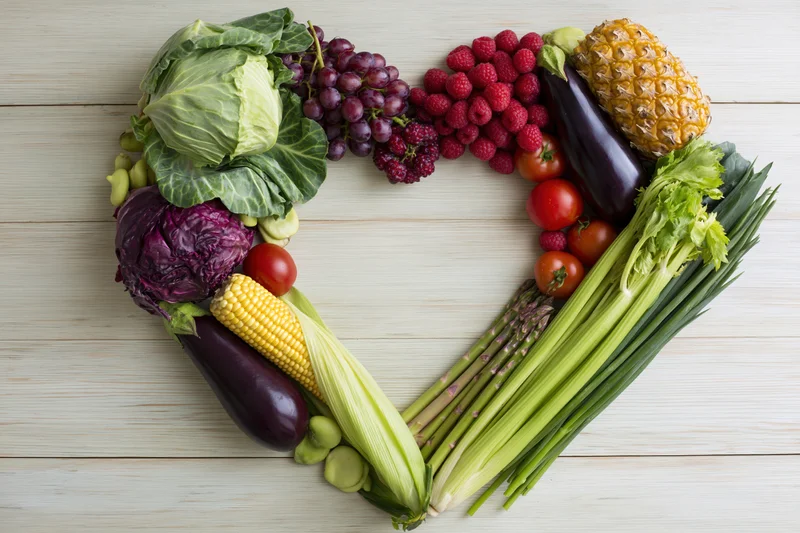 Heart-shaped arrangement of fresh vegetables and fruits on wooden surface