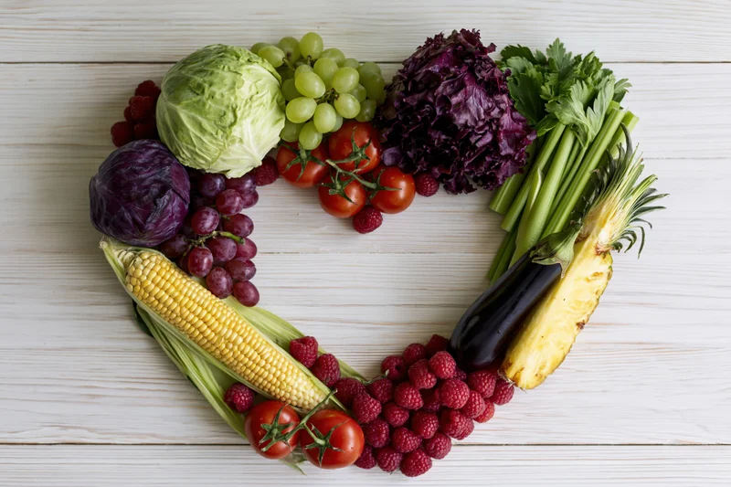 Heart-shaped arrangement of fresh fruits and vegetables on wooden surface