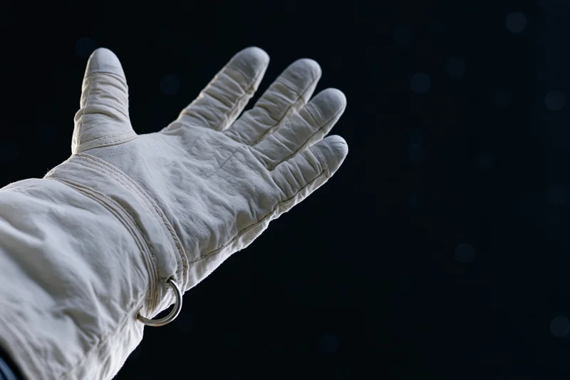 Astronaut's gloved hand extended palm-up against dark space background