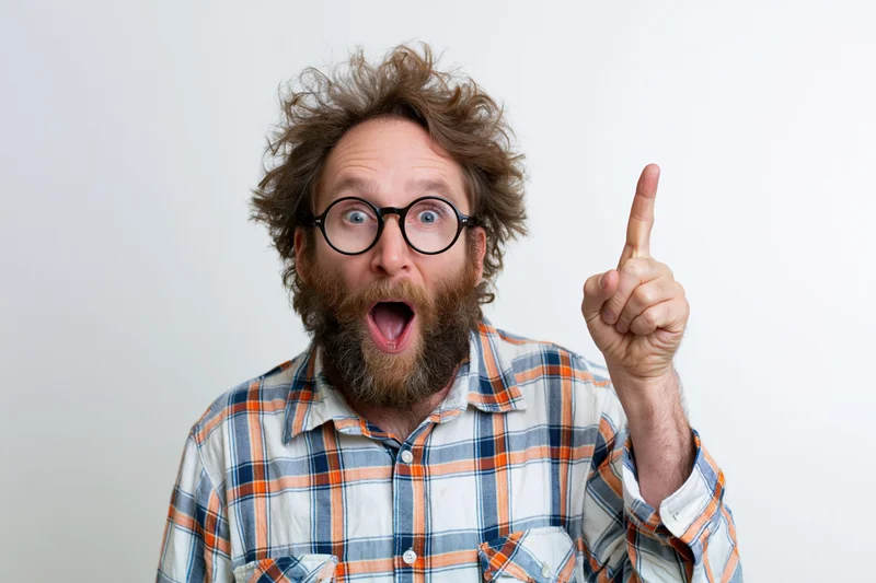Bearded man with wild hair and round glasses pointing upward in surprise against white background
