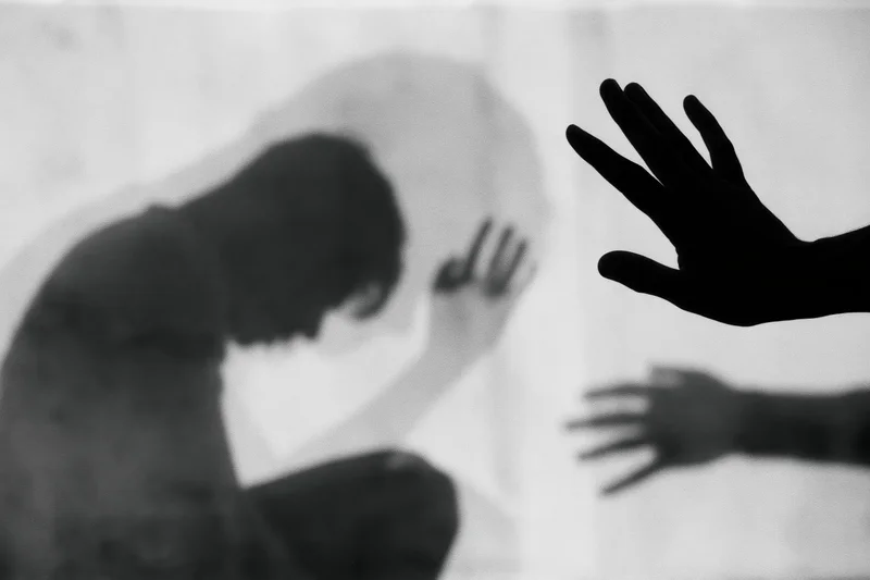 Silhouette of a distressed person with hands reaching through glass in a double exposure effect