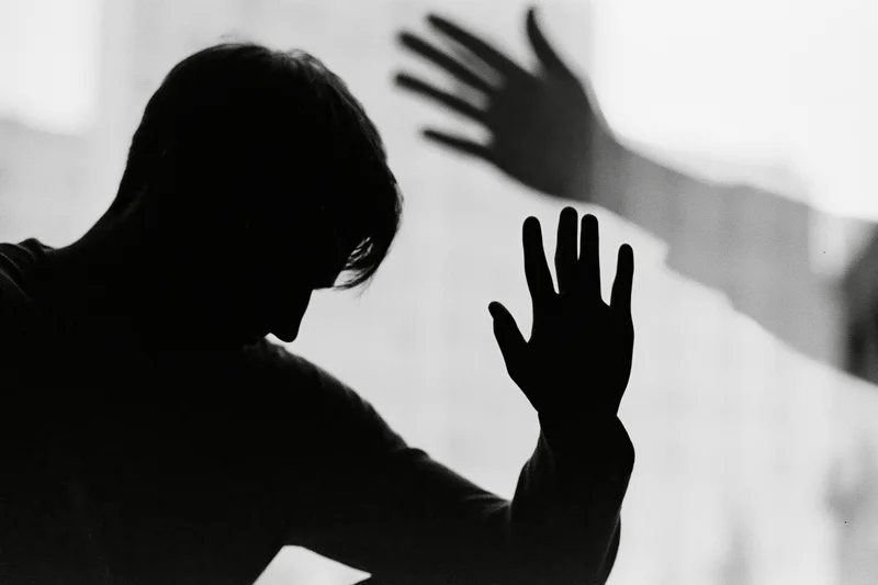 Silhouette of a distressed man reaching out with hand against a bright background
