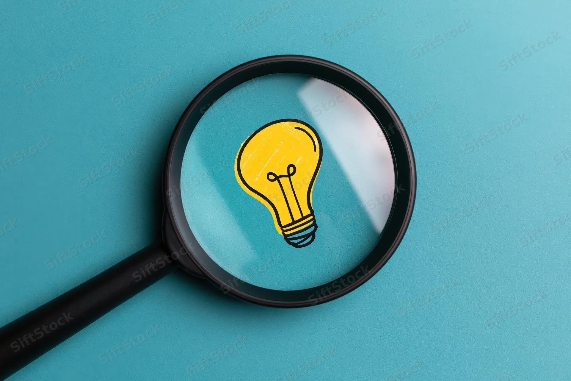 Magnifying glass focusing on a yellow lightbulb drawn on teal paper
