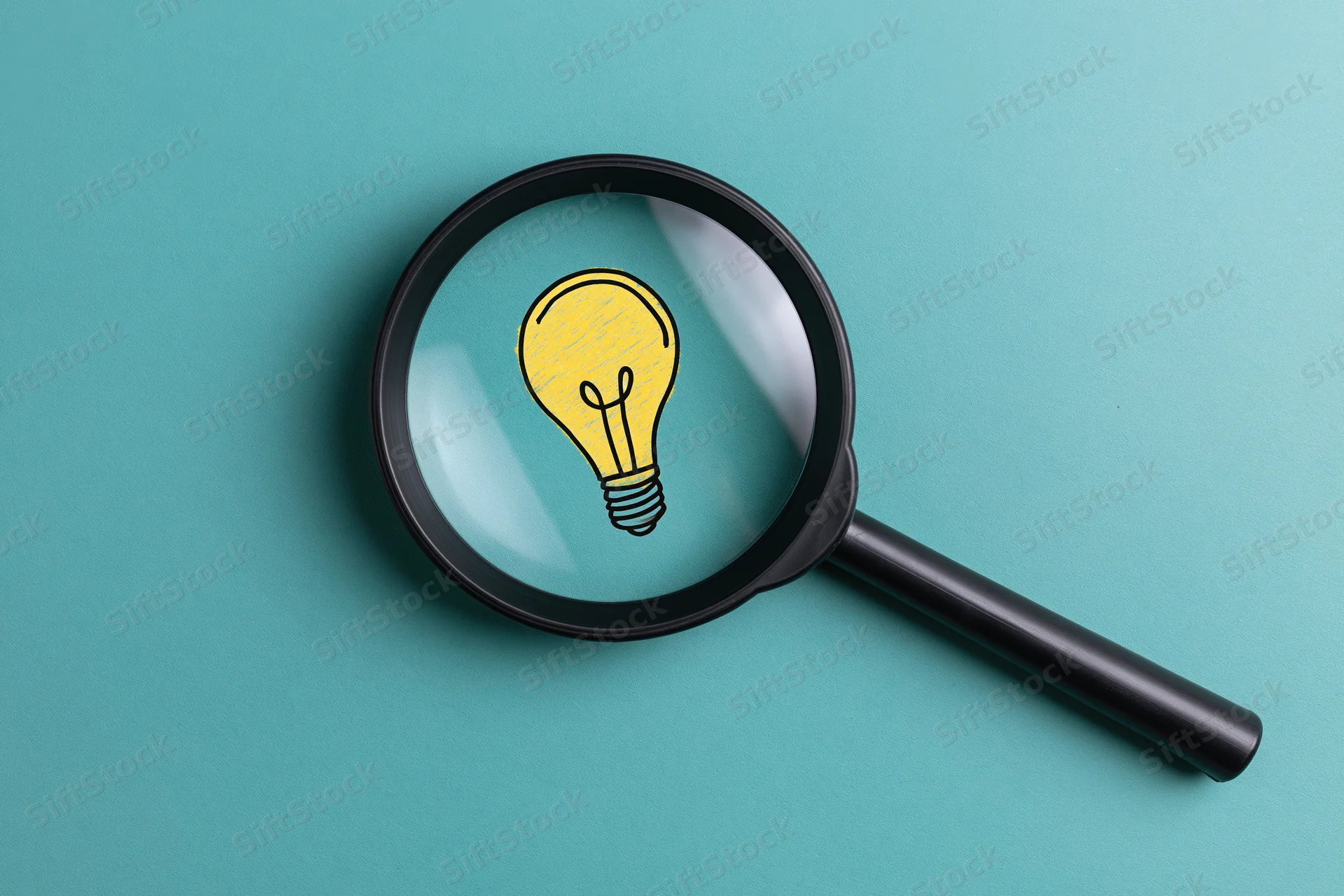 Magnifying glass focusing on a drawn lightbulb on teal background