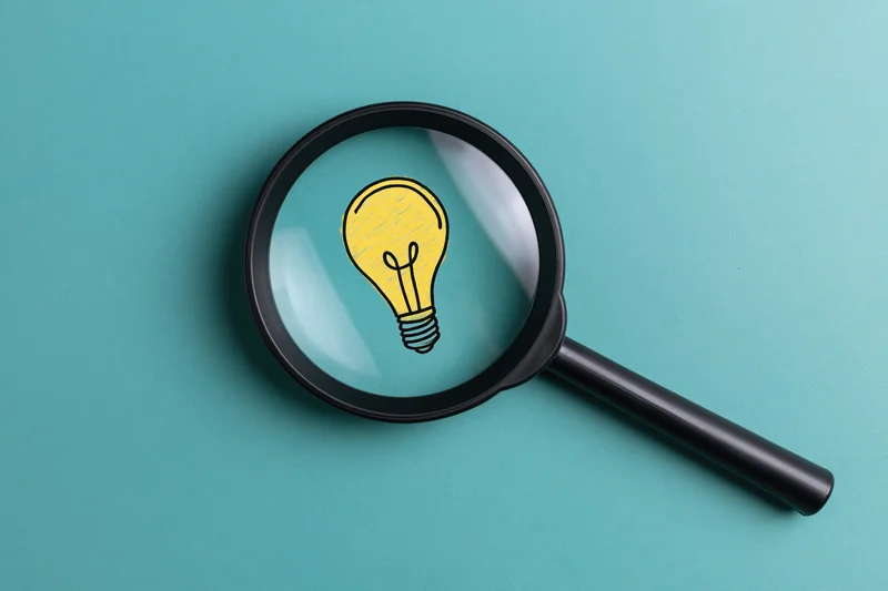 Magnifying glass focusing on a drawn lightbulb on teal background