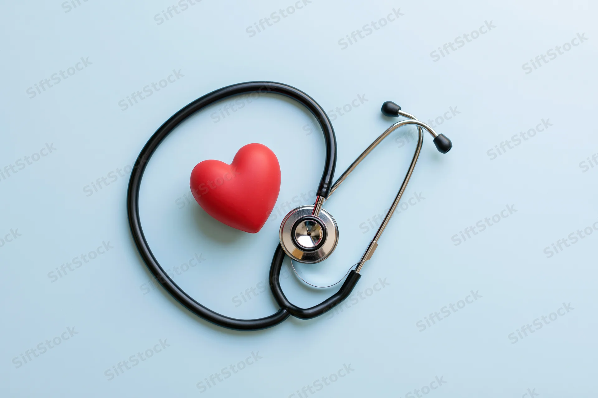 Stethoscope coiled around a red heart on a light blue surface