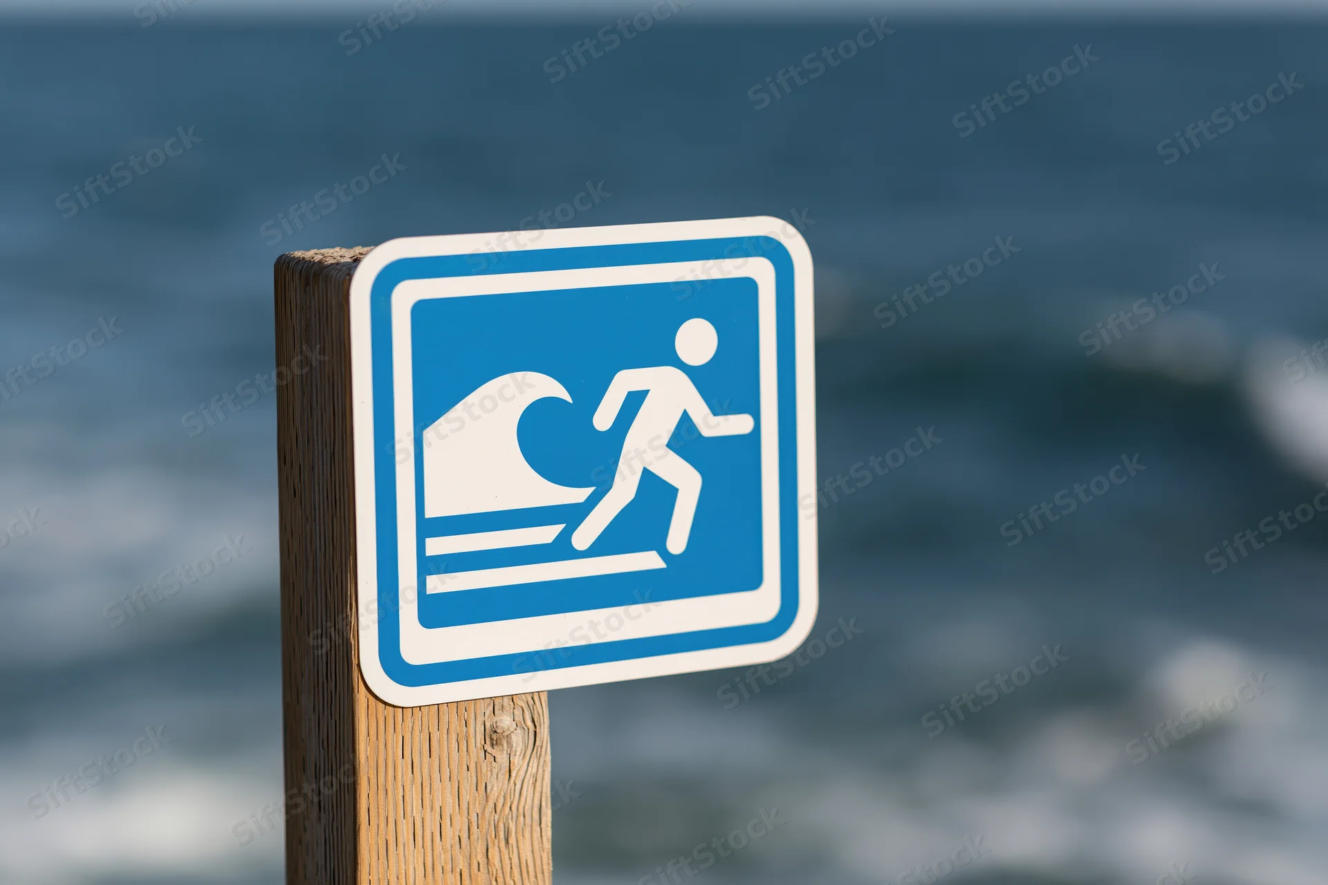 Tsunami warning sign mounted on wooden post by the ocean