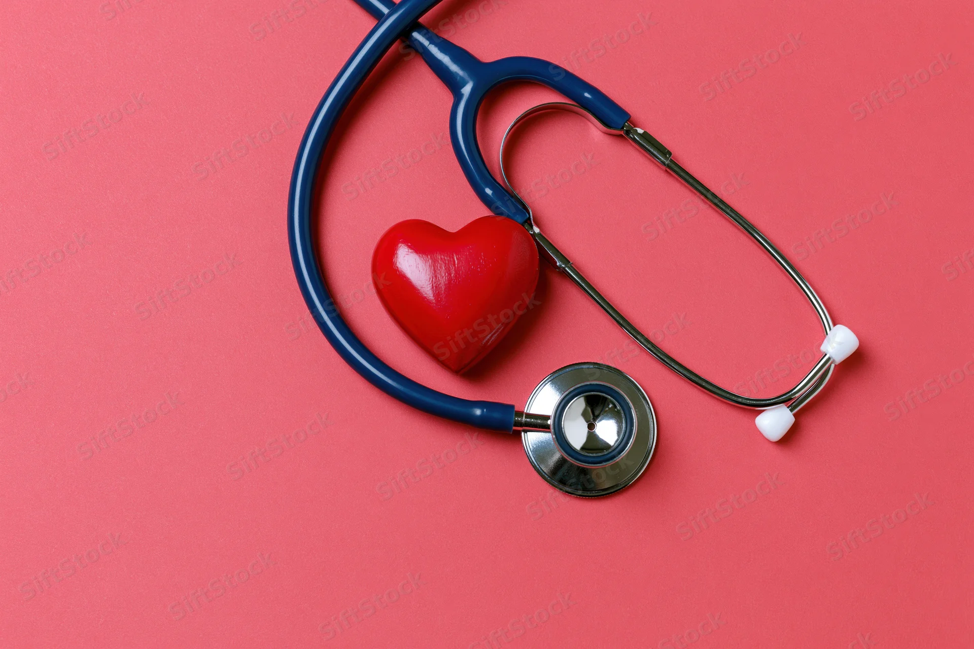 Blue stethoscope resting beside a red heart-shaped object on a pink surface