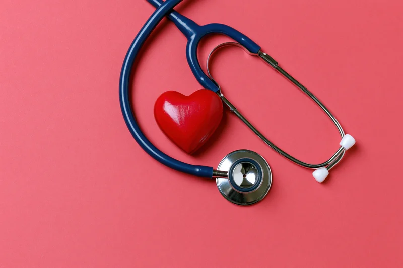 Blue stethoscope resting beside a red heart-shaped object on a pink surface