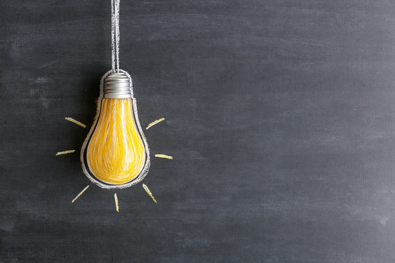 Chalk drawing of a lightbulb on a blackboard with radiating lines and copyspace to the right
