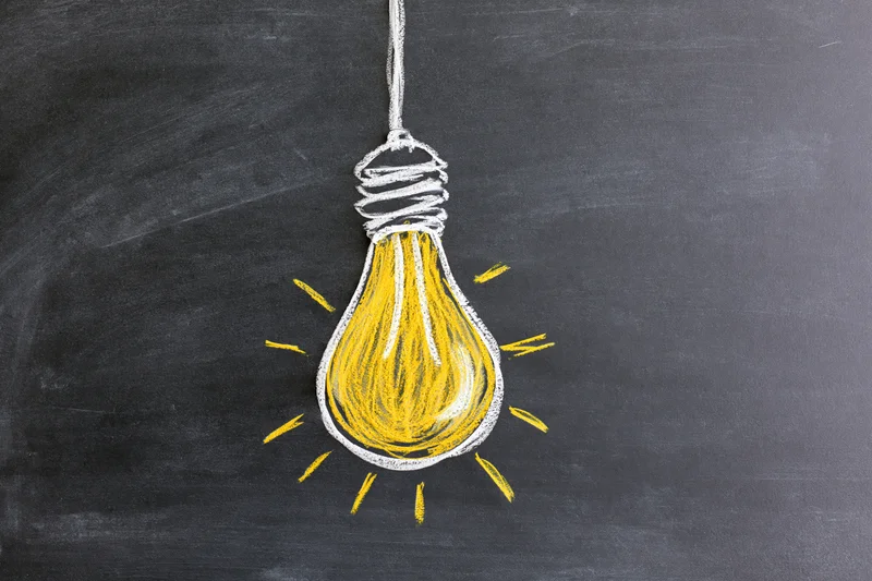 Chalk drawing of a glowing lightbulb on a blackboard surface