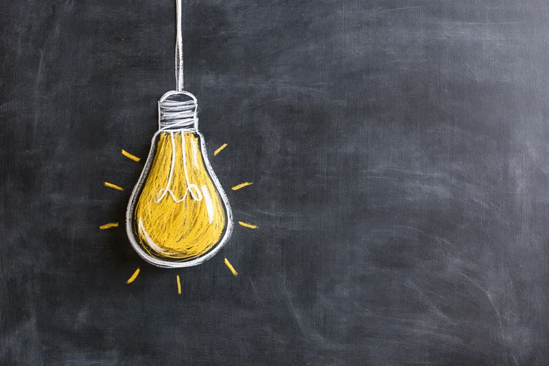 Chalk drawing of a lightbulb on a blackboard with copyspace to the right