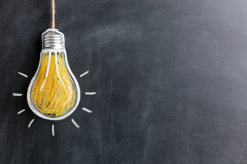 Chalk-drawn lightbulb hanging on blackboard with yellow filament and white rays