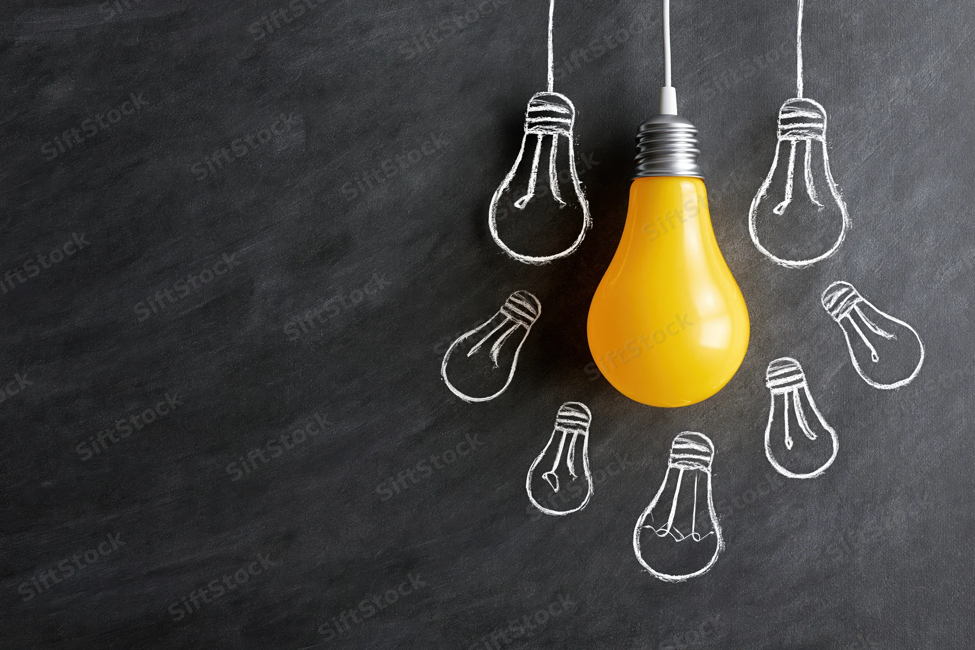 Yellow lightbulb hanging among chalk-drawn bulbs on a dark blackboard surface