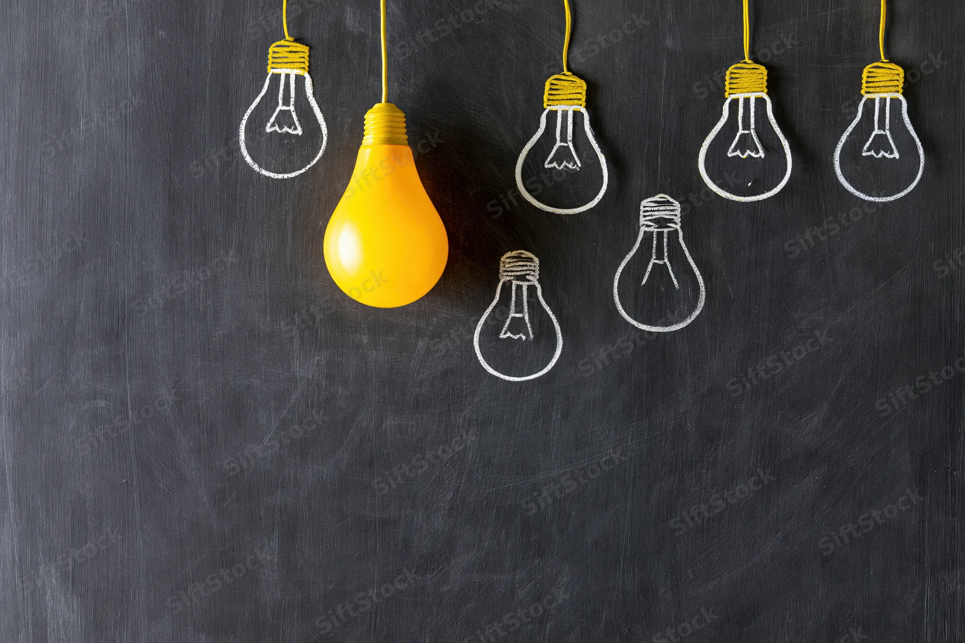 Yellow lightbulb hanging among chalk-drawn bulbs on a blackboard surface