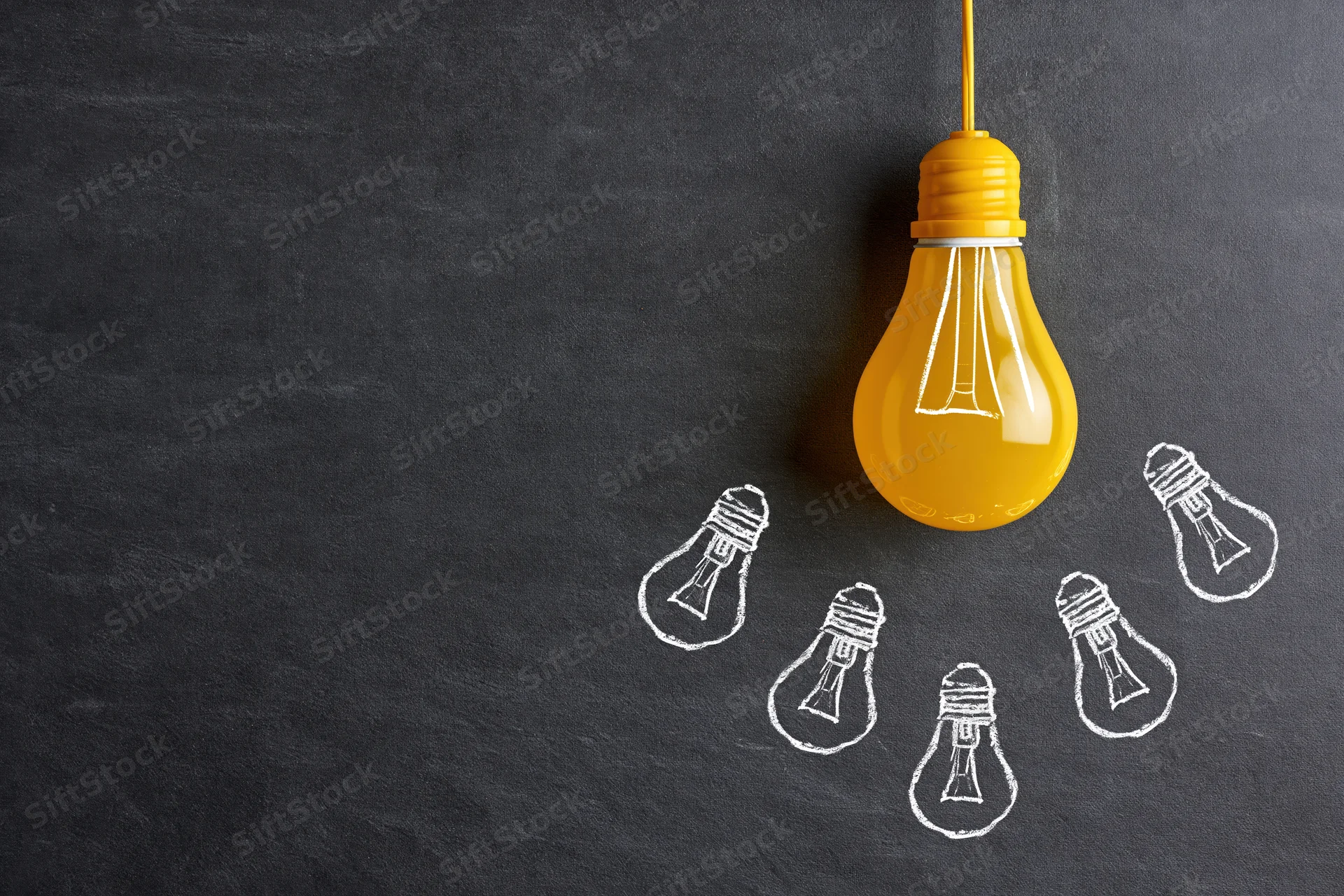 Yellow lightbulb hanging above chalk-drawn lightbulbs on a dark blackboard surface