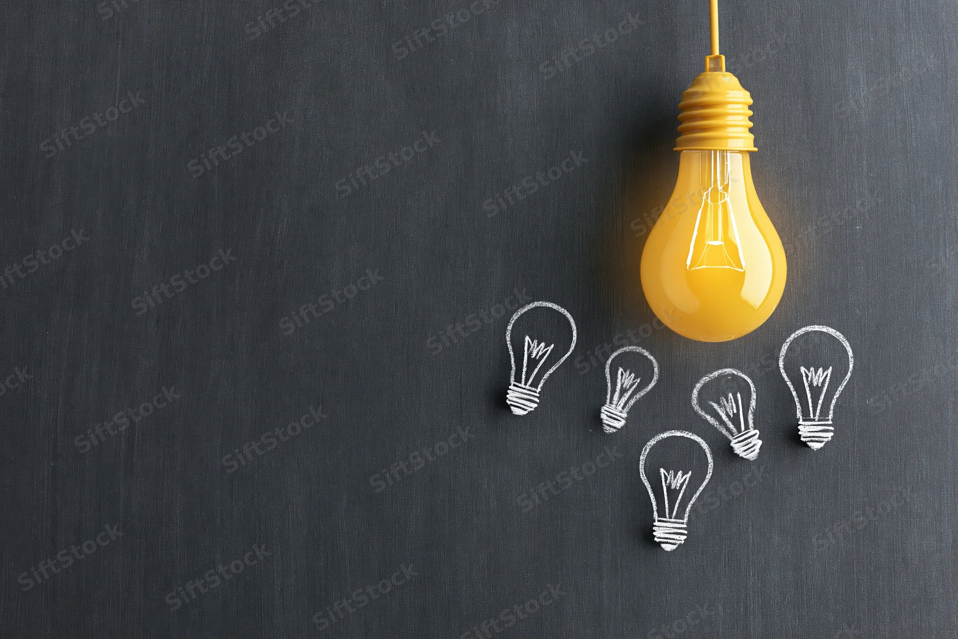 Glowing lightbulb hanging above chalk-drawn lightbulbs on a blackboard surface