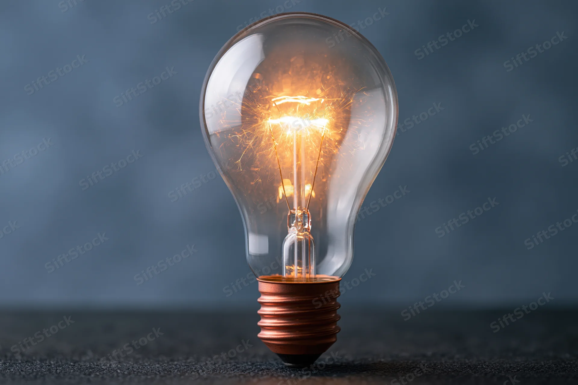 Glowing incandescent lightbulb with visible filament on dark surface