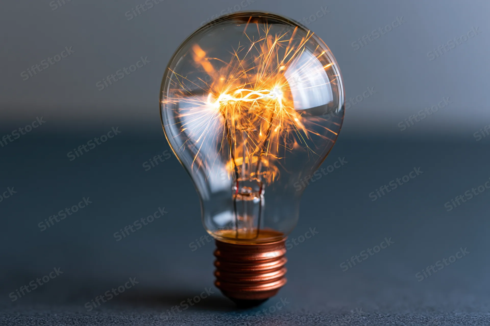 Illuminated incandescent lightbulb with sparking filament on dark surface