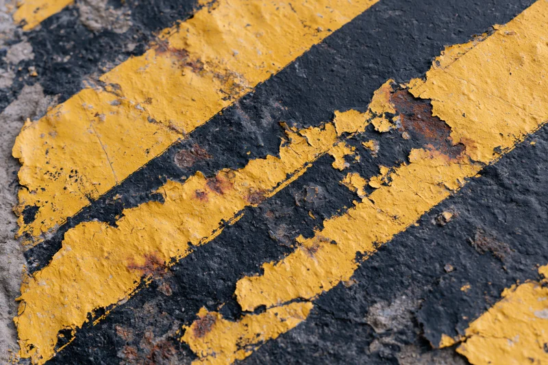 Close-up of peeling yellow stripes on weathered asphalt pavement