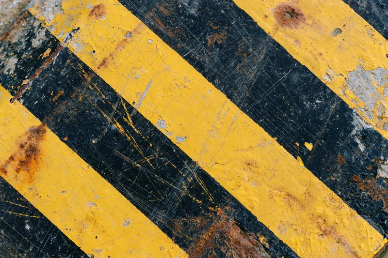 Weathered yellow and black hazard stripes on a corroded metal surface