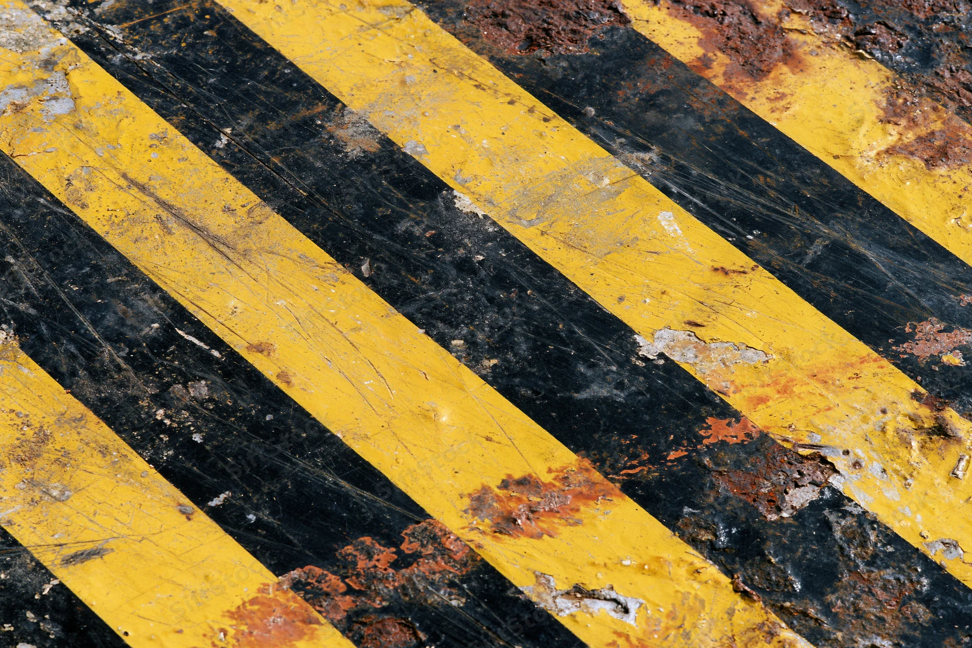 Weathered yellow and black diagonal hazard stripes on a rusted metal surface
