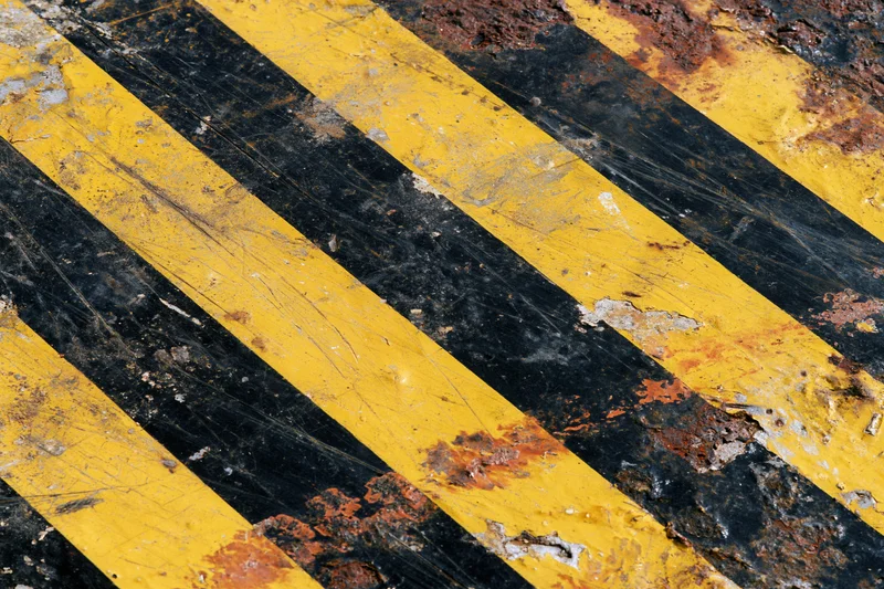 Weathered yellow and black diagonal hazard stripes on a rusted metal surface