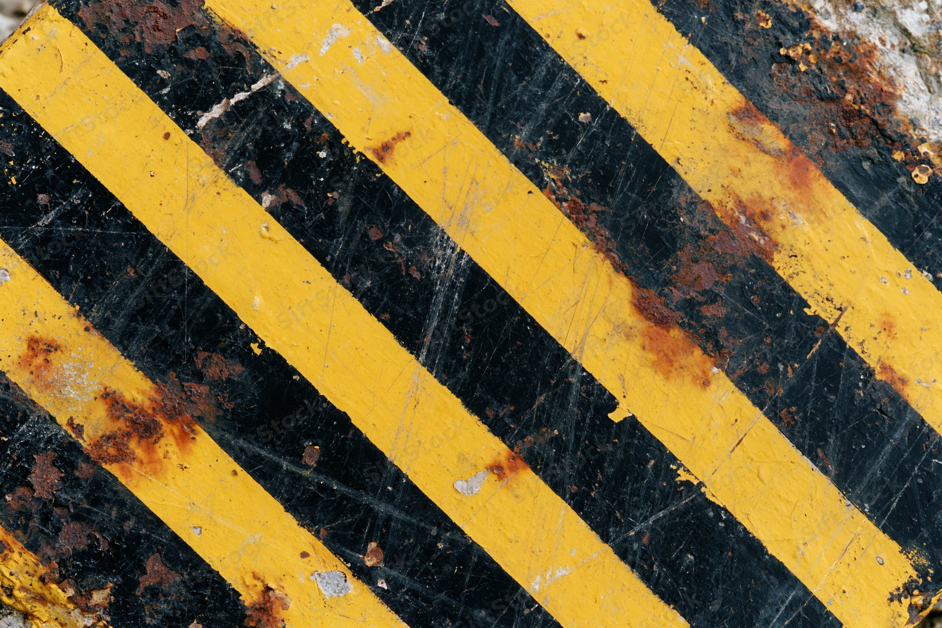 Close-up of weathered yellow and black hazard stripes on a rusty metal surface