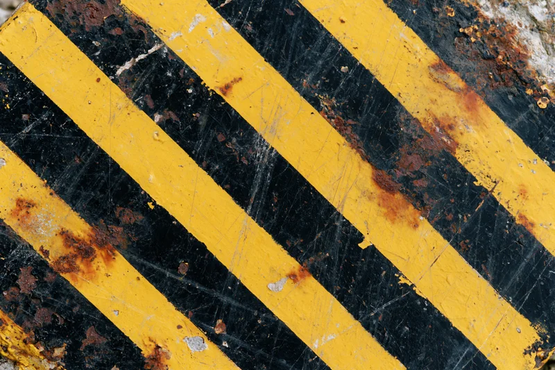 Close-up of weathered yellow and black hazard stripes on a rusty metal surface