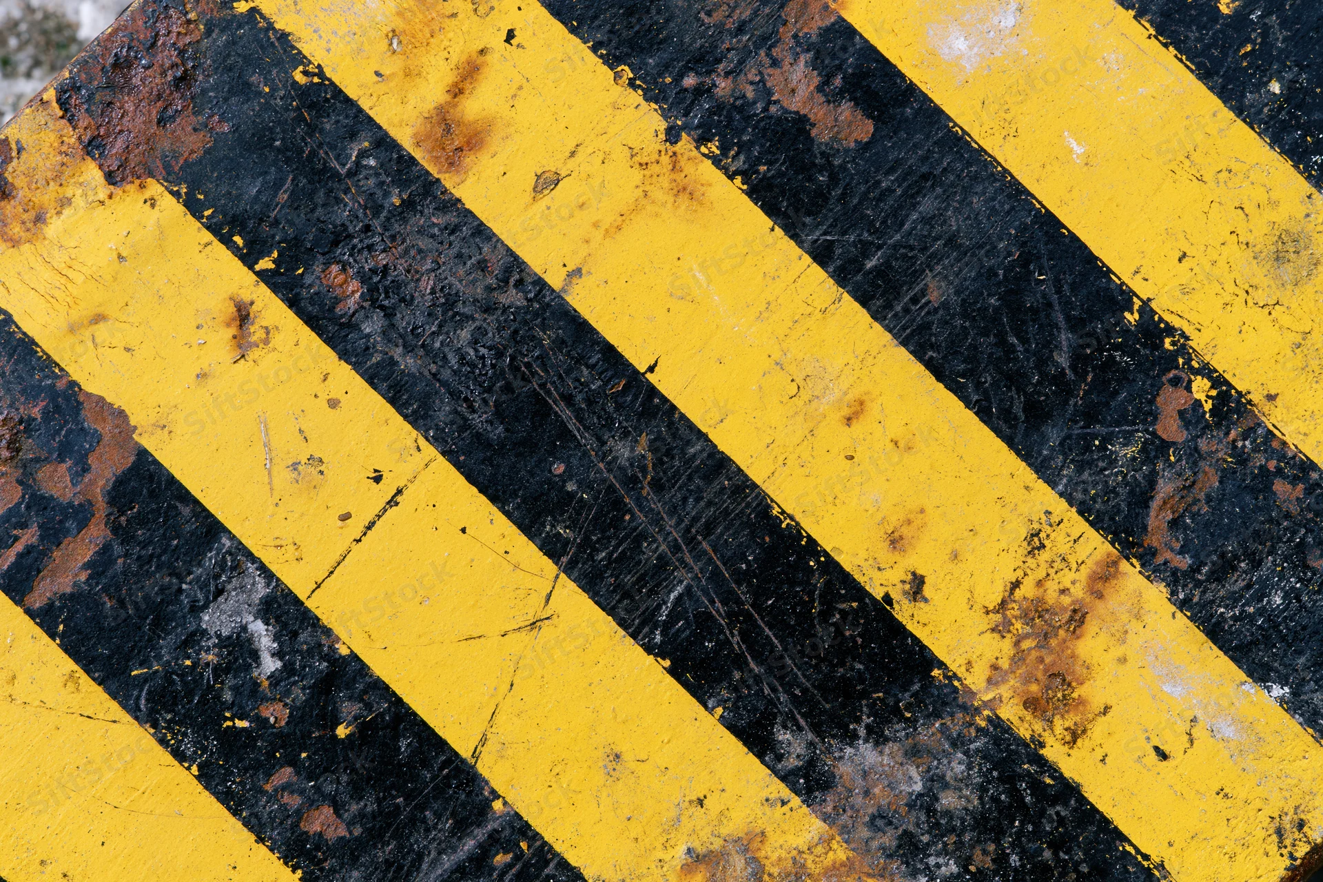 Close-up of weathered yellow and black diagonal hazard stripes on a corroded metal surface