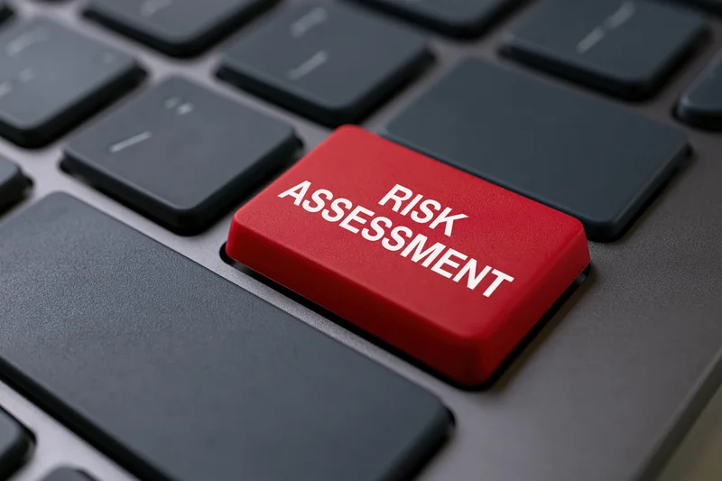 Red button labeled risk assessment on dark grey laptop keyboard closeup