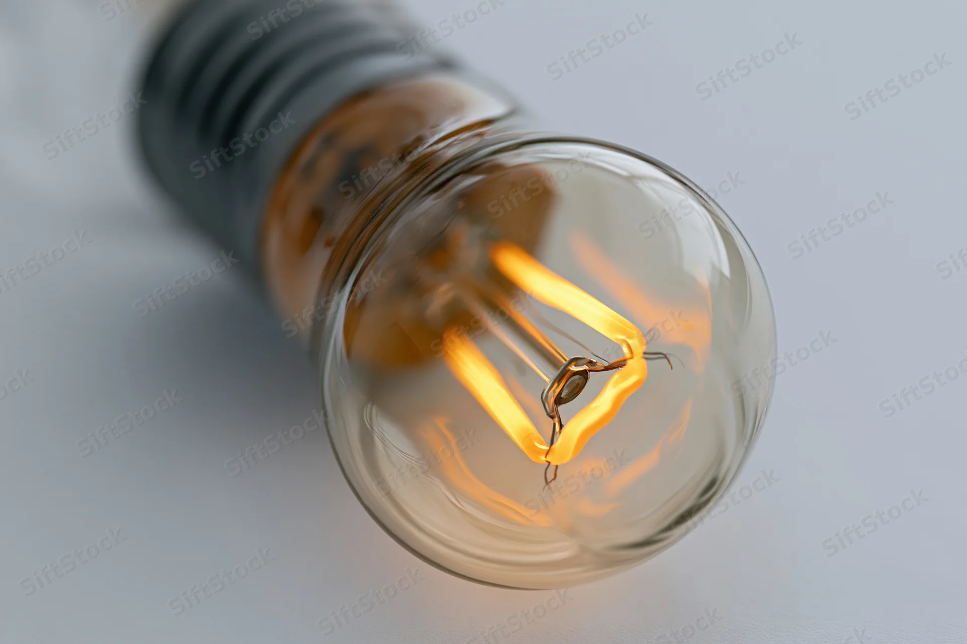 Glowing incandescent light bulb with visible filament lying on a white surface