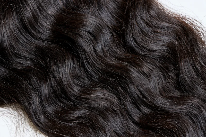 Close-up of dark black wavy human hair extensions on white background