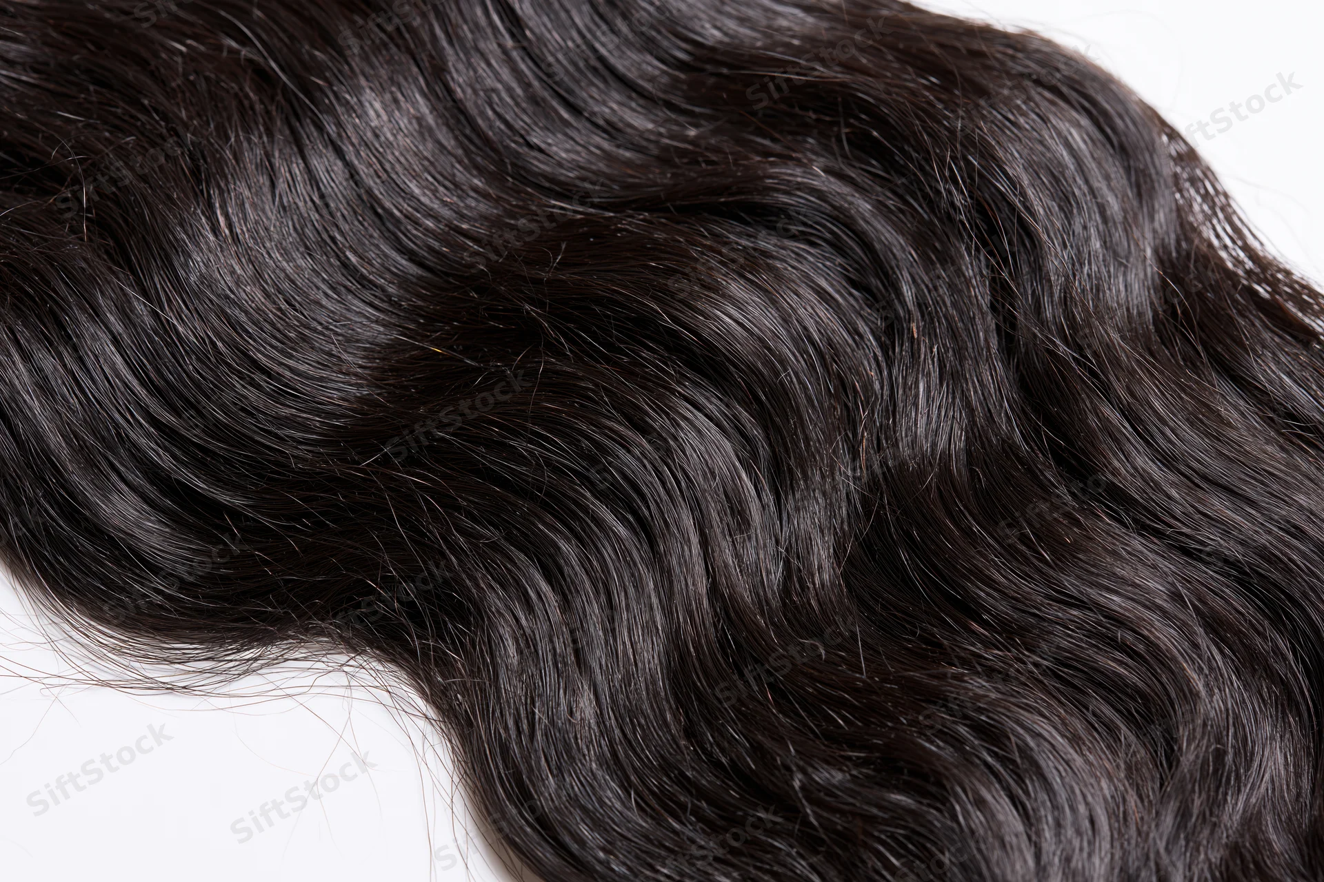 Close-up of dark black wavy human hair extensions on white background