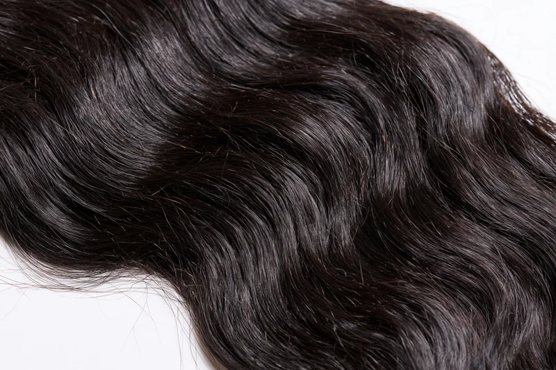 Close-up of dark black wavy human hair extensions on white background