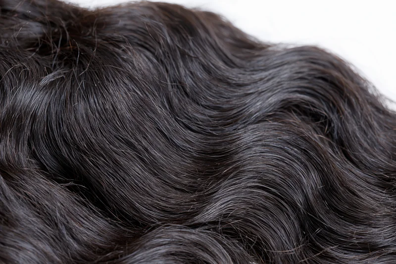 Close-up of dark wavy human hair extensions on white background