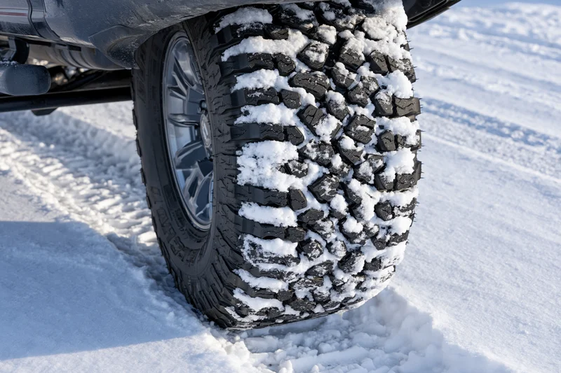 Close-up of a black all-terrain truck tire packed with snow on a snowy ground
