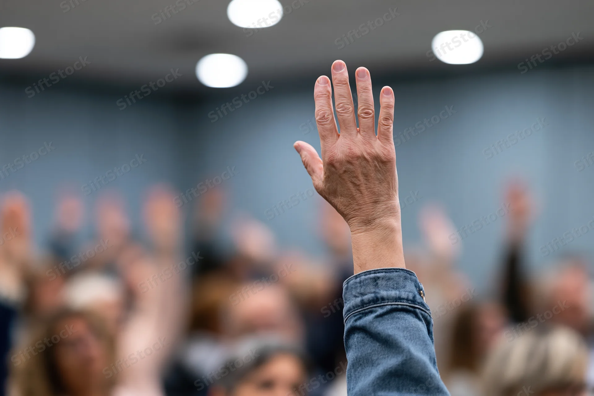 Raised hand in foreground during group meeting with audience in background